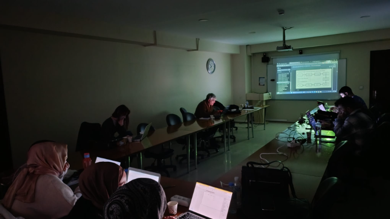 Teknik eğitimde U düzeni masa başında çalışan katılımcılar, projeksiyonla sunum izliyor.